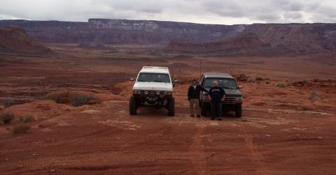 1990 Ford Bronco - Two off-road SUVs parked in a desert landscape with two men standing beside them.