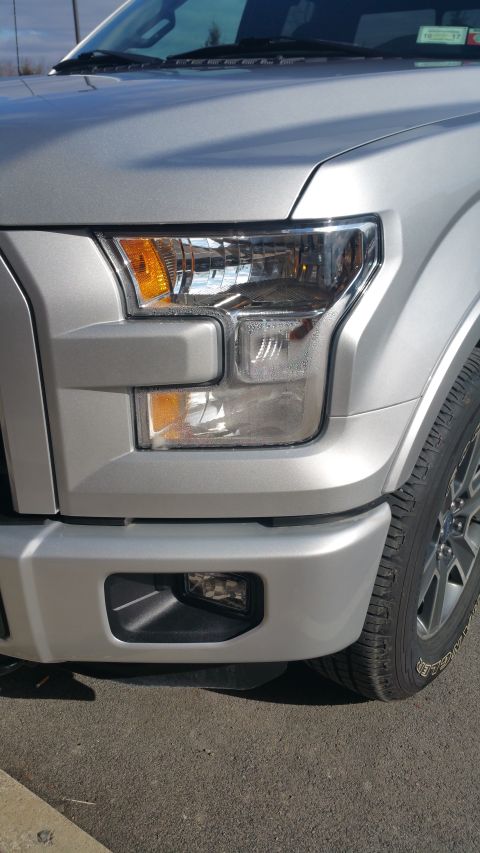 2015 Ford F-150 - Close-up of the front passenger side of a silver pickup truck, highlighting the headlight assembly and fog light.
