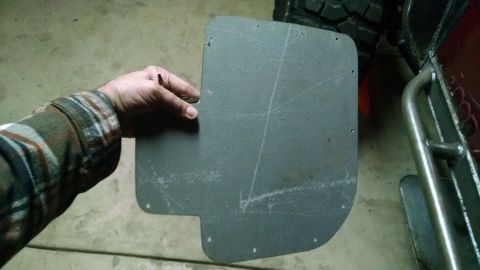 1985 Jeep CJ7 - A custom mud flap is held up, showing scribe lines for cutting and mounting holes. The vehicle it is intended for is partially visible.