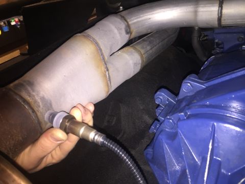 1982 Ford Bronco - An oxygen sensor is held near a Y-shaped exhaust pipe, with a blue component visible in the background.