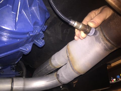 1982 Ford Bronco - An oxygen sensor is being installed into the exhaust system, with a blue transmission housing visible.