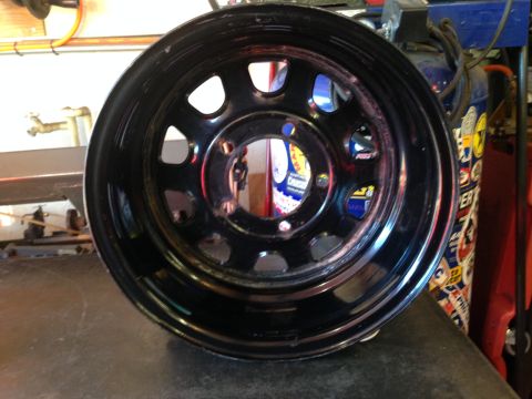 1987 Suzuki Samurai - A close-up view of a black steel wheel, likely for an off-road vehicle, with visible reflections in its surface.