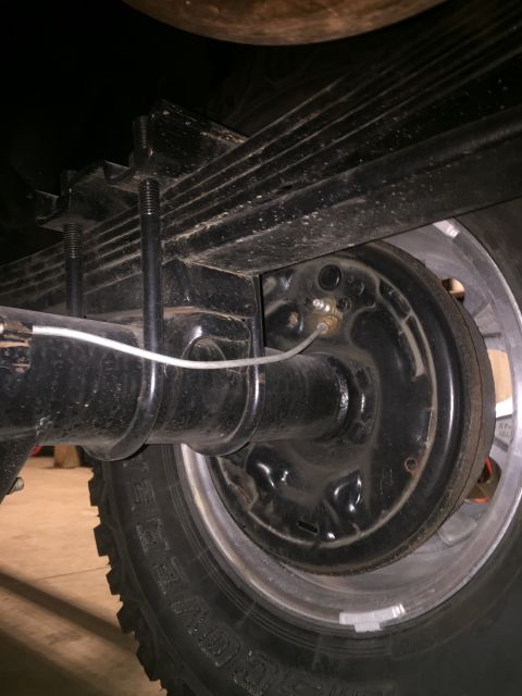 1982 Ford Bronco - Close-up view of a vehicle's rear axle, leaf springs, and drum brake system.