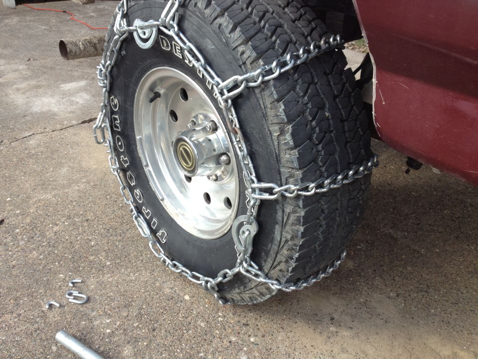 Maroon vehicle's front tire with snow chains installed on concrete