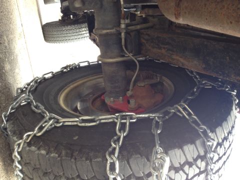 1996 Ford Bronco - Snow chains are installed on a vehicle's tire and axle for traction in winter conditions.