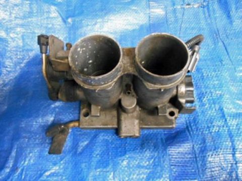 1990 Ford Bronco - A dual throttle body part is shown against a blue tarp background.