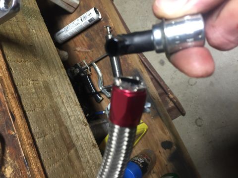1982 Ford Bronco - A mechanic works on a braided hose with a socket wrench, with tools and a tube on a wooden surface.