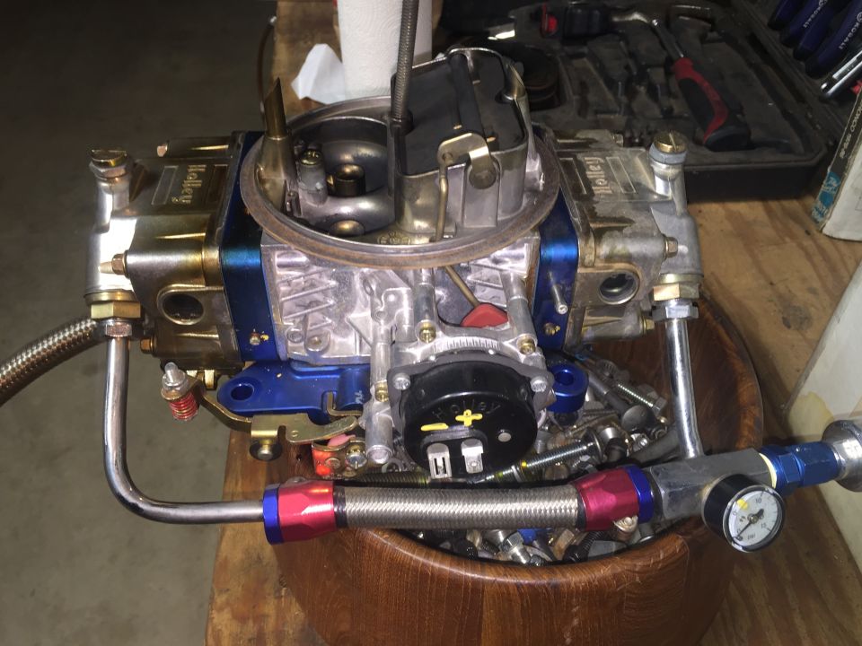 Holley carburetor with blue accents and braided fuel lines, resting in a wooden bowl