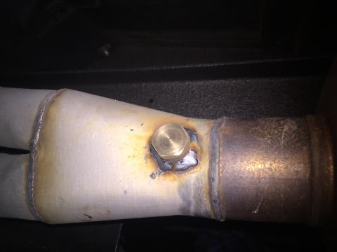 1982 Ford Bronco - A close-up of a welded exhaust pipe modification featuring a brass plug. The pipe shows signs of heat discoloration and rust.