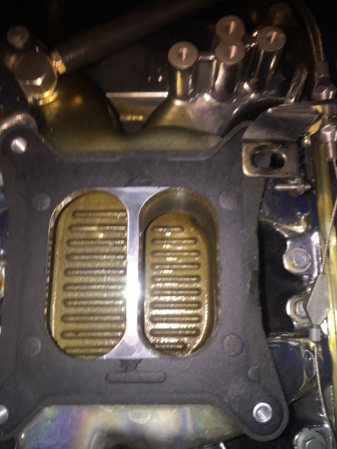 1982 Ford Bronco - A close-up view of a carburetor intake manifold gasket with a chrome intake manifold visible above it. The gasket has two large oval openin…