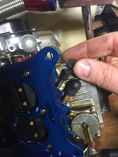 1982 Ford Bronco - A close-up view of a hand holding small black rubber parts over a blue-coated carburetor assembly.