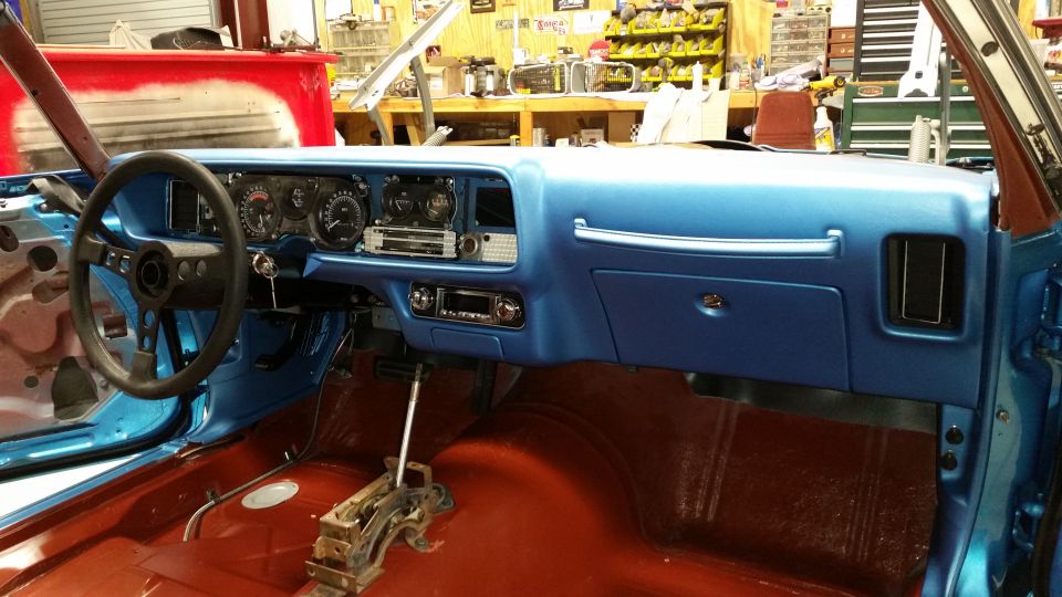 Interior of a blue classic car dashboard with steering wheel, gauges, and stereo.