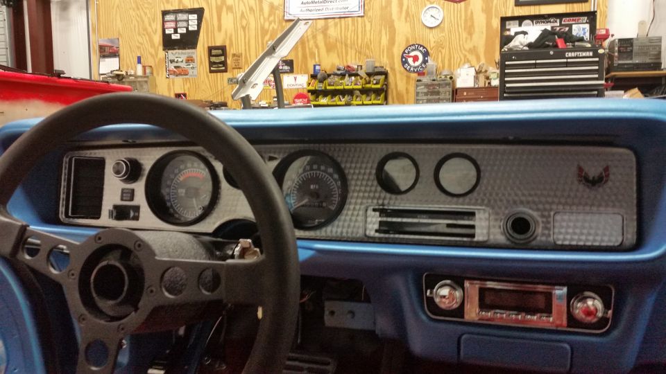 Interior of a blue 1970 Pontiac Trans Am dashboard with steering wheel, gauges, and Firebird emblem.