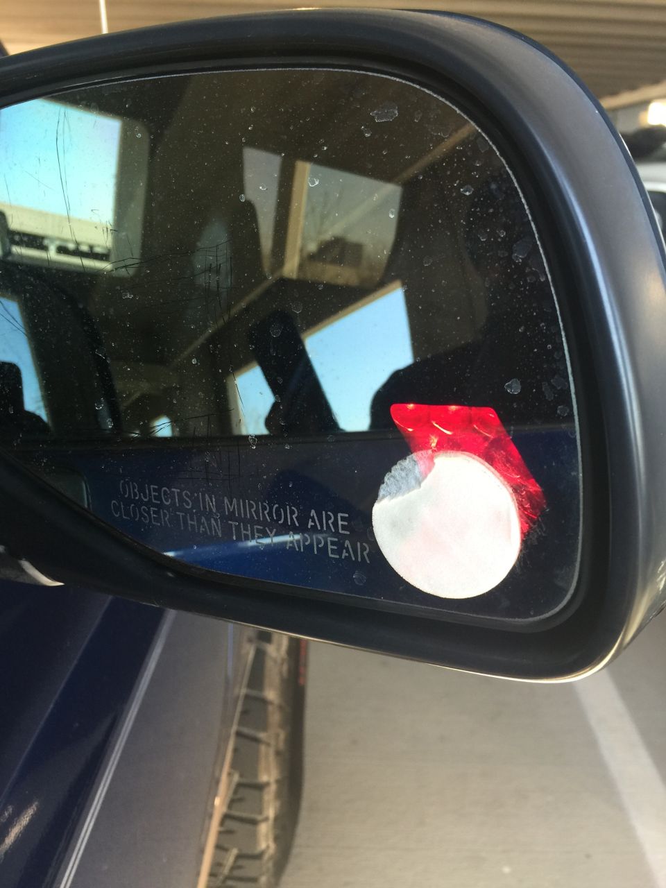 Driver's side mirror of a blue vehicle with a warning sticker and a partial sticker.