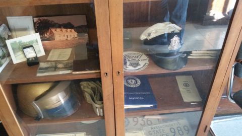 1991 Ford LTD Crown Victoria - Photograph of wooden display cases filled with police hats, helmets, photos, manuals and license plates.