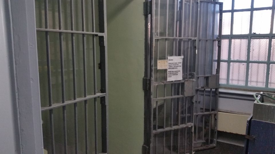 Interior view of old jail cells with steel bars and a posted notice
