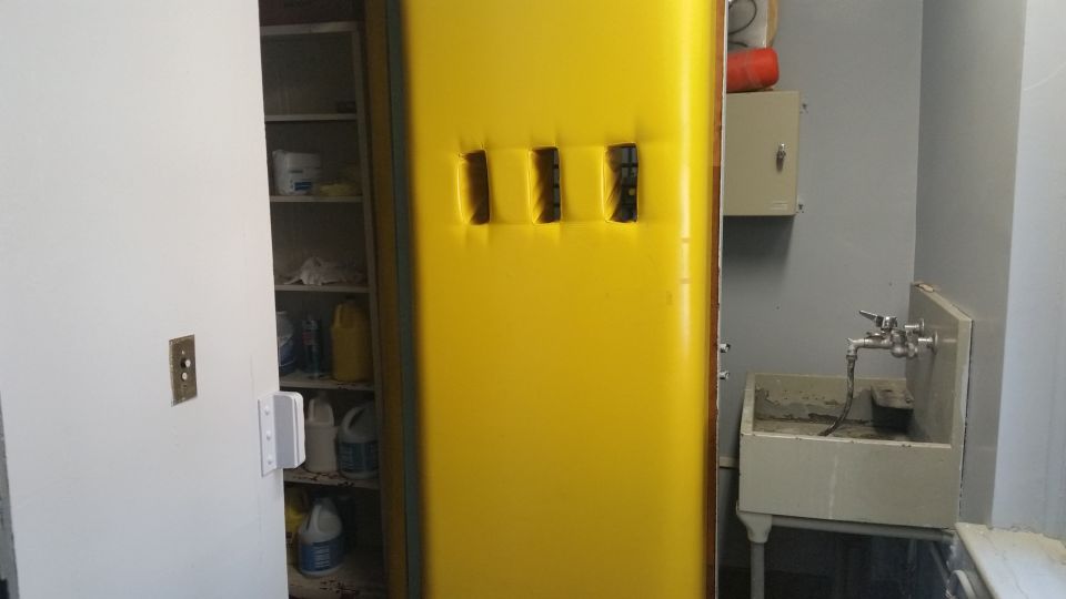 Yellow flammable storage cabinet beside a sink and shelving in a utility room