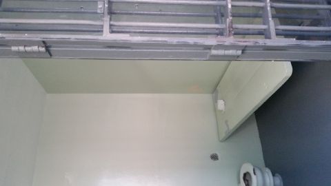 1991 Ford LTD Crown Victoria - Photo of a jail cell interior with a stainless toilet, wall-mounted bunk and gray barred door.