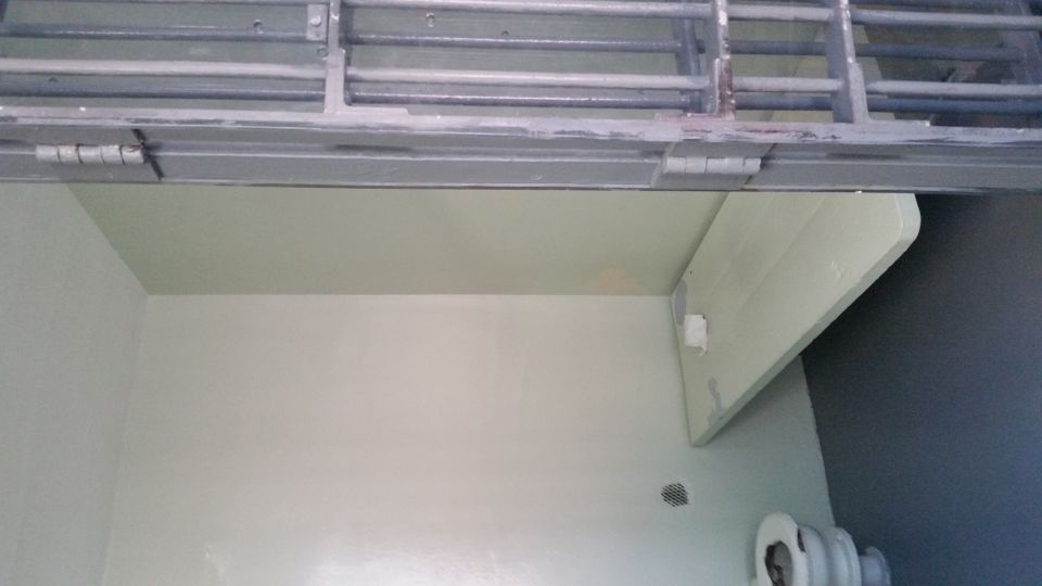 Jail cell interior with toilet, wall-mounted bunk and barred door