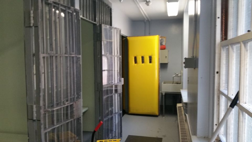 Jail corridor with barred cells, yellow locker and sink
