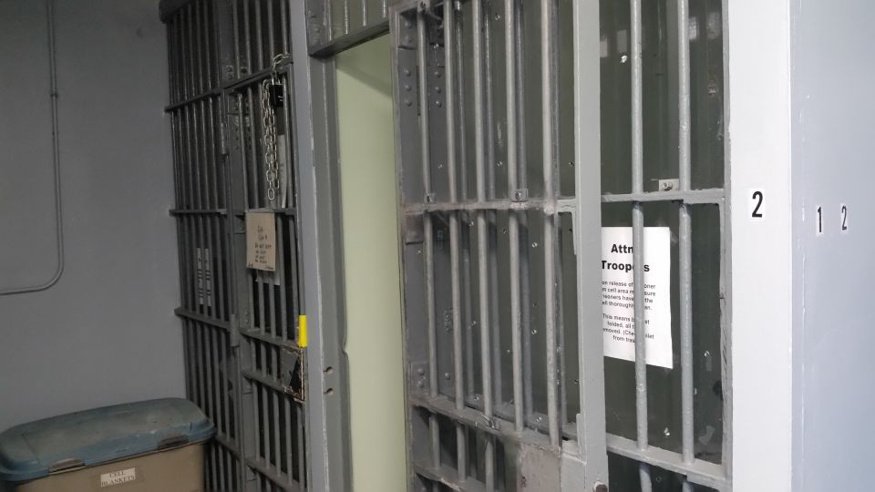 Barred jail cell door with padlock and chain and a posted notice
