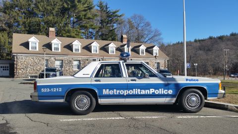 1991 Ford LTD Crown Victoria - Photo of a Metropolitan Police Ford LTD Crown Victoria cruiser, side profile at a stone police station.