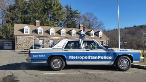 1991 Ford LTD Crown Victoria - Photo of a Metropolitan Police Ford LTD Crown Victoria cruiser parked outside a stone police station.