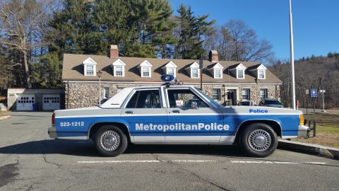1991 Ford LTD Crown Victoria - Photo of a blue and white Metropolitan Police Ford Crown Victoria cruiser parked at a stone station.