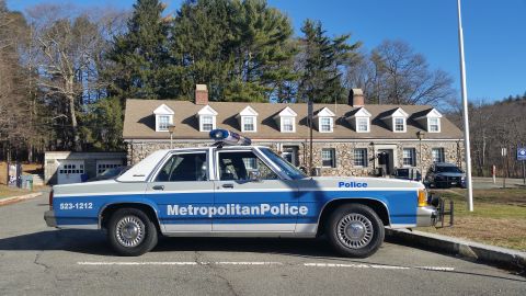 1991 Ford LTD Crown Victoria - Photo of a vintage Metropolitan Police Ford Crown Victoria cruiser parked before a stone police station.