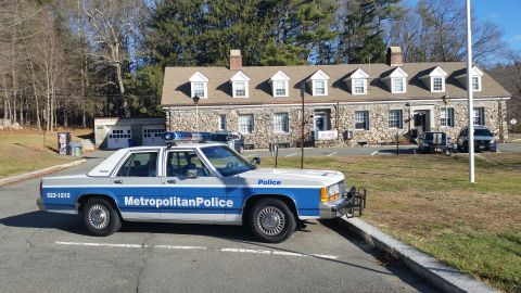 1991 Ford LTD Crown Victoria - Photo of a Metropolitan Police Ford Crown Victoria cruiser parked outside a stone police station.