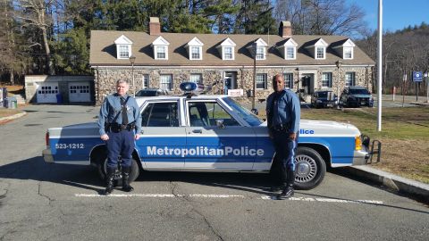 1991 Ford LTD Crown Victoria - Photo of two officers posing beside a Metropolitan Police Ford Crown Victoria cruiser at a stone station.