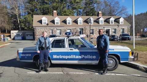 1991 Ford LTD Crown Victoria - Photo of two officers standing by a Metropolitan Police Ford Crown Victoria cruiser outside a station.