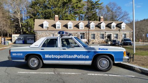 1991 Ford LTD Crown Victoria - Photo of a Metropolitan Police Ford Crown Victoria cruiser parked before a stone police station.