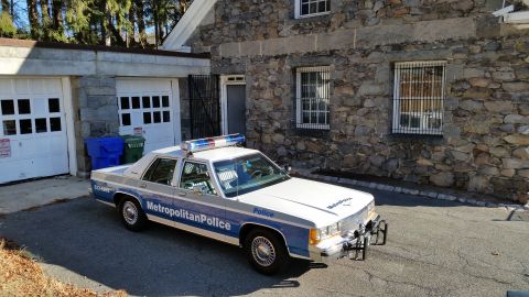 1991 Ford LTD Crown Victoria - Photo of a Metropolitan Police Ford Crown Victoria cruiser parked in a driveway beside a stone building.