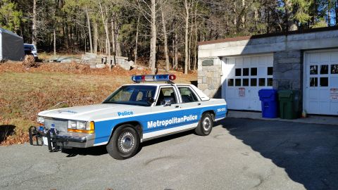 1991 Ford LTD Crown Victoria - Photo of a vintage Ford Metropolitan Police patrol car parked beside garage doors, not a technical document.