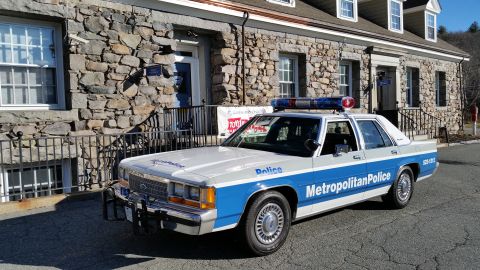 1991 Ford LTD Crown Victoria - Photo of a vintage Ford Metropolitan Police patrol car parked in front of a stone building, not a technical document.