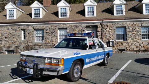 1991 Ford LTD Crown Victoria - Photo of a vintage Ford Metropolitan Police patrol car parked at a stone station building, not a technical document.