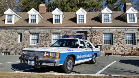 1991 Ford LTD Crown Victoria - Photo of a vintage Ford Metropolitan Police patrol car parked before a dormered stone building, not a technical document.