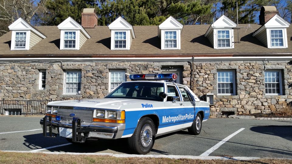 Metropolitan Police Ford sedan parked before dormered stone building