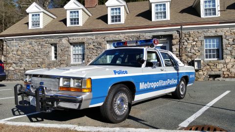 1991 Ford LTD Crown Victoria - Photo of a vintage Ford Metropolitan Police patrol car with push bar in a parking lot, not a technical document.