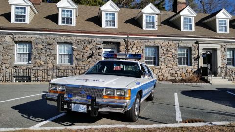 1991 Ford LTD Crown Victoria - Photo of a vintage Ford Metropolitan Police patrol car parked head-on at a stone station, not a technical document.