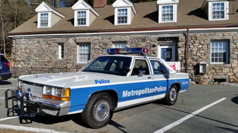 1991 Ford LTD Crown Victoria - Photo of a vintage Ford Metropolitan Police patrol car parked in front of a stone station building, not a technical document.