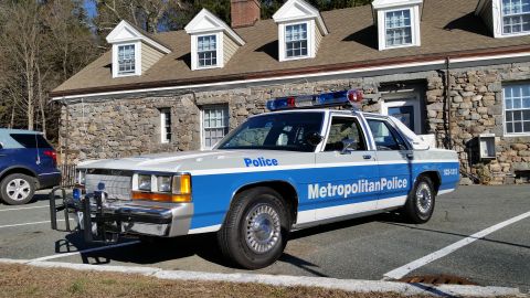 1991 Ford LTD Crown Victoria - Photo of a vintage Ford Metropolitan Police patrol car with push bar at a stone building, not a technical document.