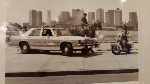 1991 Ford LTD Crown Victoria - Sepia photo showing a police cruiser, mounted officer, and motorcycle officer with a city skyline, not a technical document.