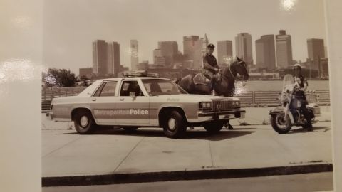 1991 Ford LTD Crown Victoria - Sepia photo of a police cruiser, mounted officer, and motorcycle officer before a skyline, not a technical document.
