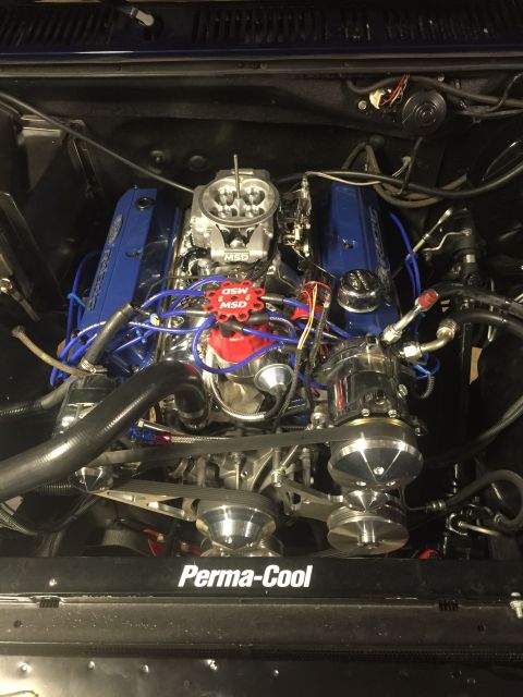 1982 Ford Bronco - A close-up, overhead view of a highly modified V8 engine bay. Visible parts include blue Ford Racing valve covers, a chrome carburetor, MSD…