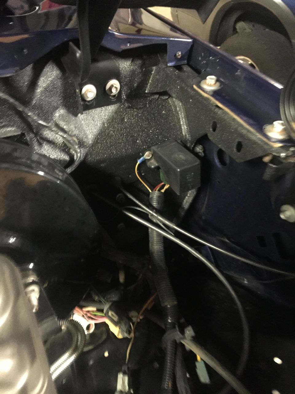Engine bay wiring and electrical box in a dark blue vehicle.