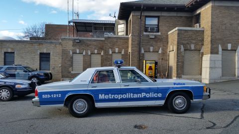 1991 Ford LTD Crown Victoria - Photo of a blue-and-white Metropolitan Police Crown Victoria parked beside a brick building, not a technical document.