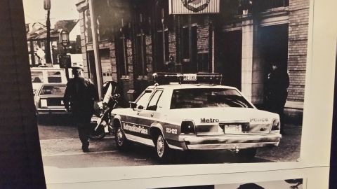 1991 Ford LTD Crown Victoria - A 1991 Ford Crown Victoria police car is seen from the rear, parked outside a building with a police officer walking nearby.