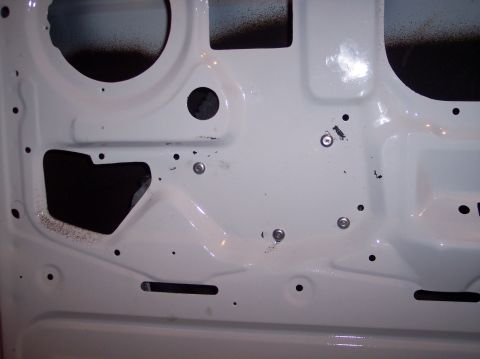1990 Ford Bronco - The interior of a white vehicle door shows exposed metal and screw holes, with some overspray visible.